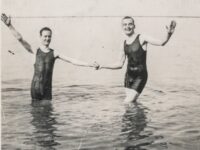 Two men in full swimsuits holding hands vintage
