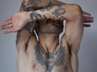 Half naked man covering face with wing tattoo on chest