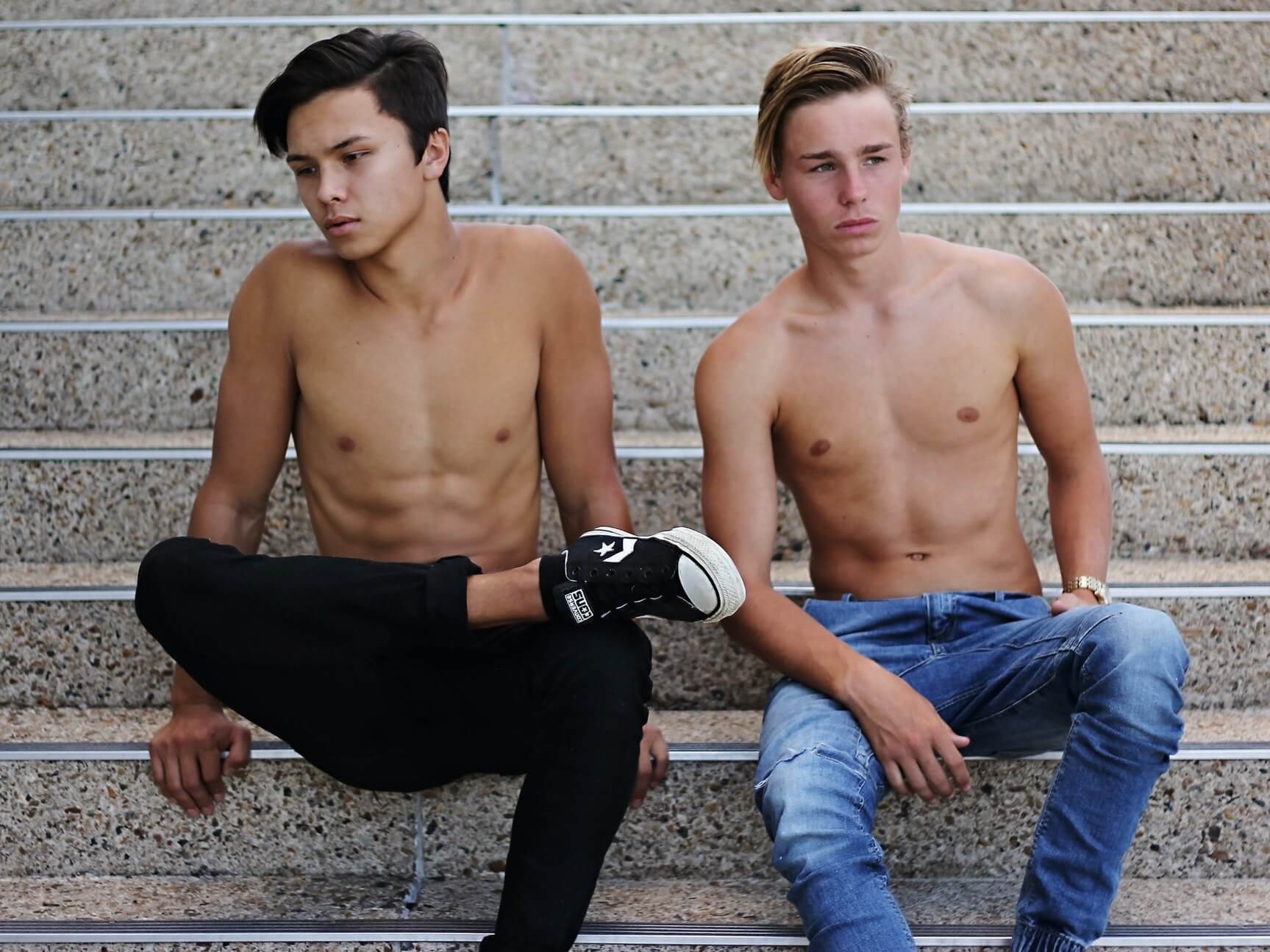 Two shirtless young men sitting on stairs