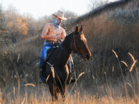 Shirtless cowboy with bandana riding on horse
